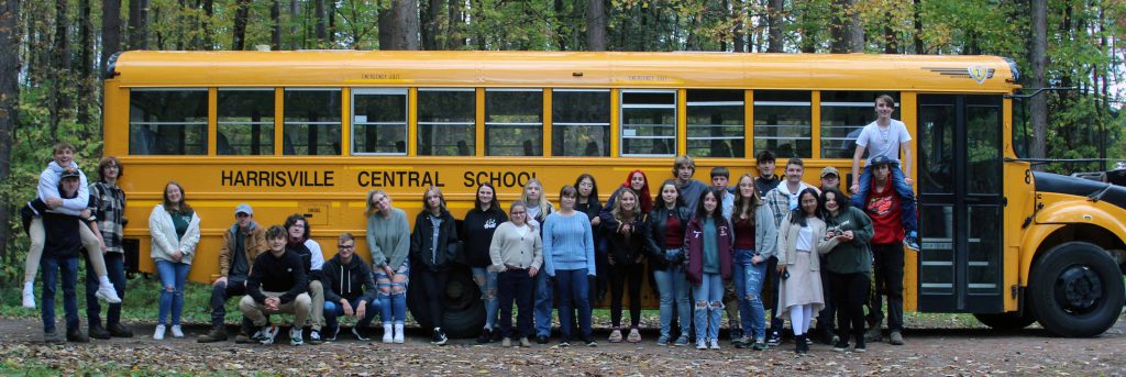 Image of several high school-aged students posing for a photo in front of a school bus that is labeled as Harrisville Central School