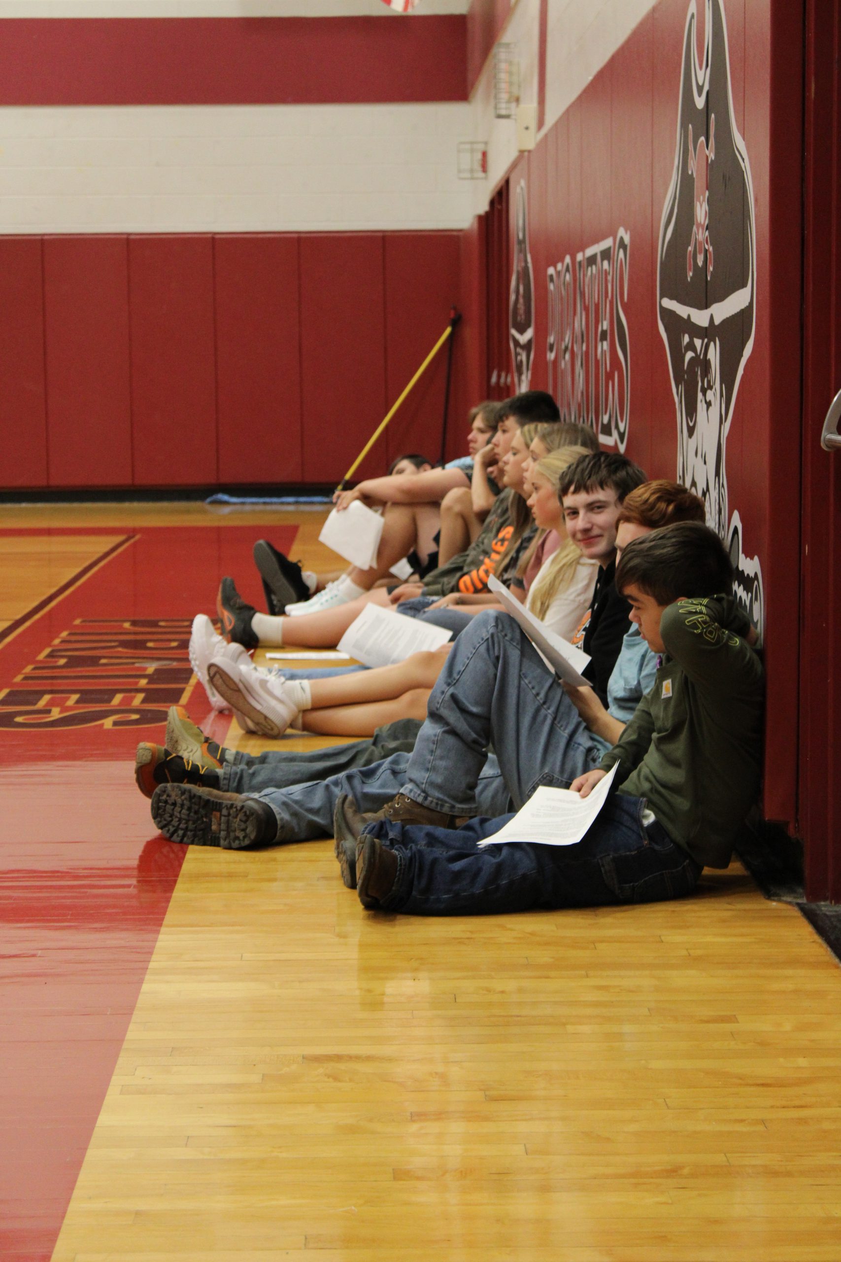 Image of an adult sitting with several students on a gymnasium floor