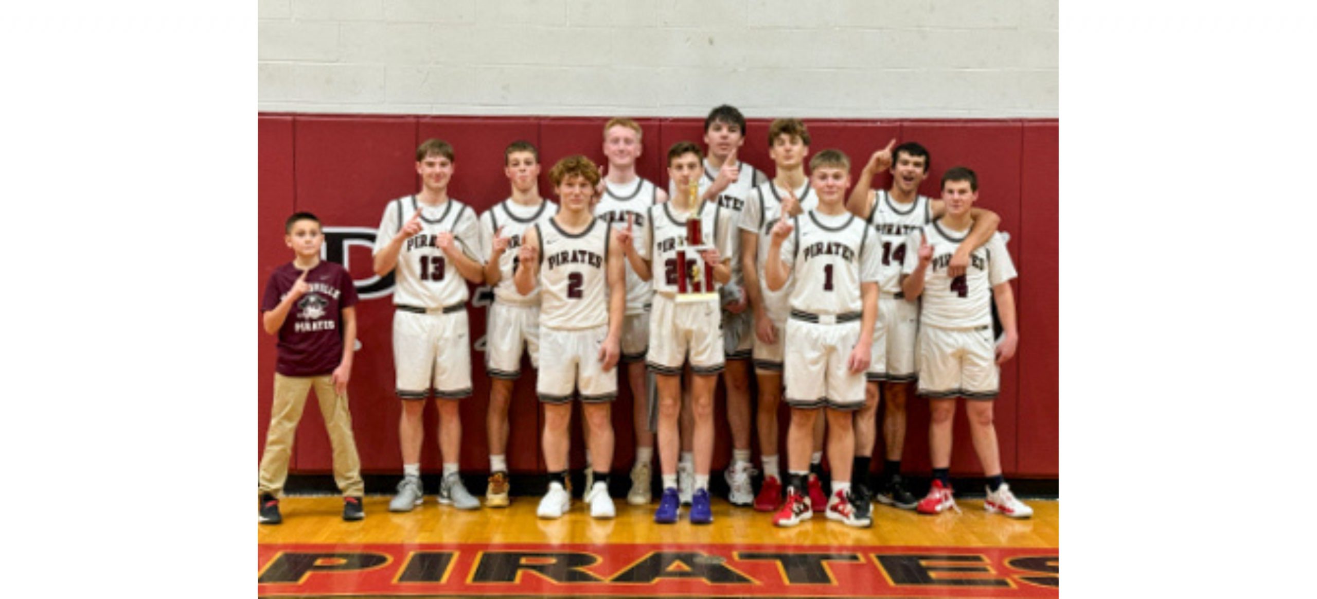 A group of 11 boys standing in basketball jerseys in a gymnasium posing for a photograph