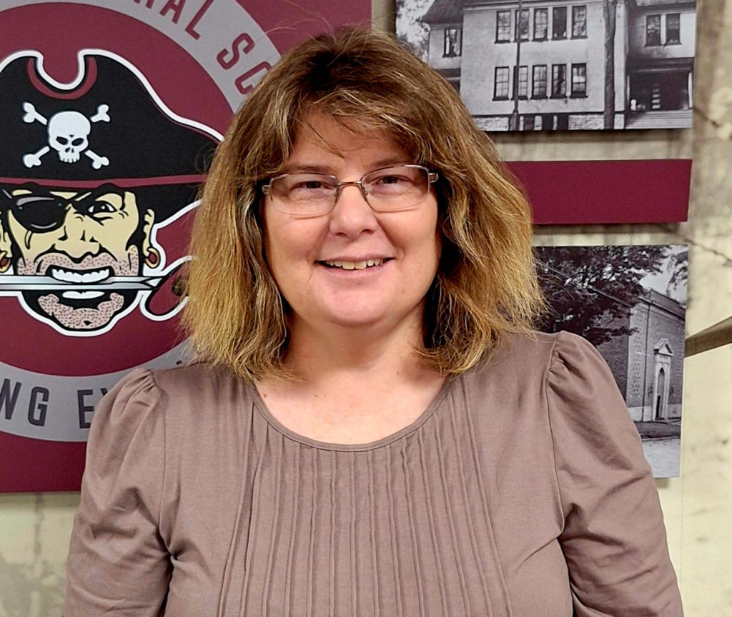 A woman smiling for a photo standing in front of a wall with photos and a pirate logo