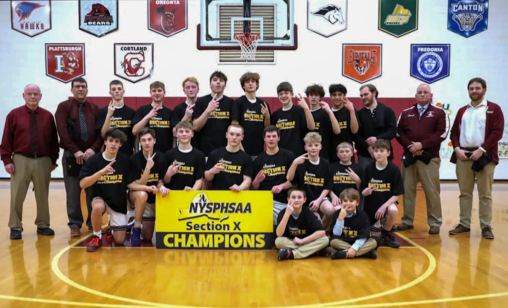 A group of 18 boys along side five adults in a gymnasium posing for a photograph